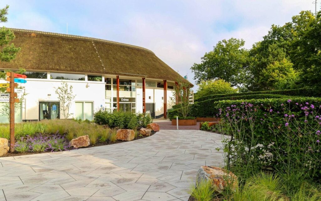 Entree van een golfbaan in Heelsum met een tegelplein en siergrassen voor het clubhuis met rieten kap