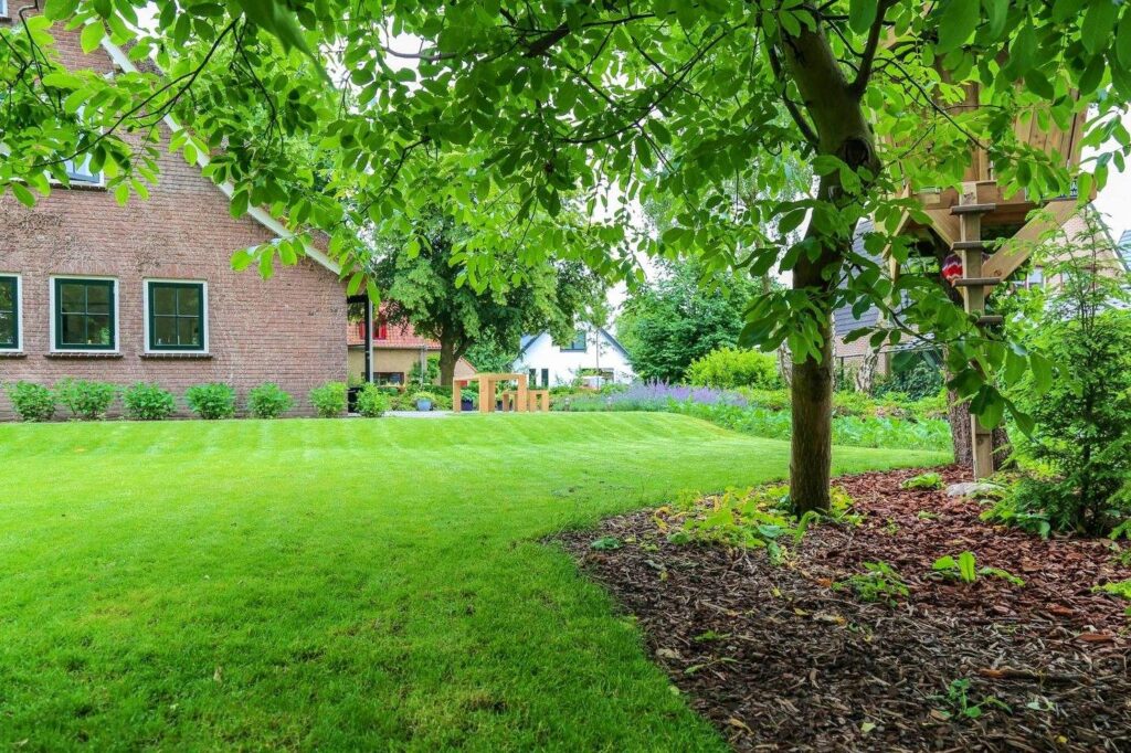Gazon met boomschors rond een boom in een grote landelijke tuin in Bennekom