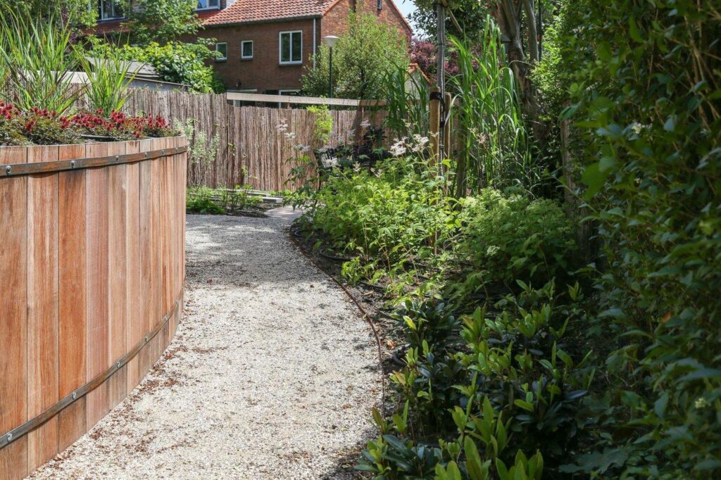 Grindpad langs een houten keerwand en hoge beplanting in een achtertuin in Oosterbeek