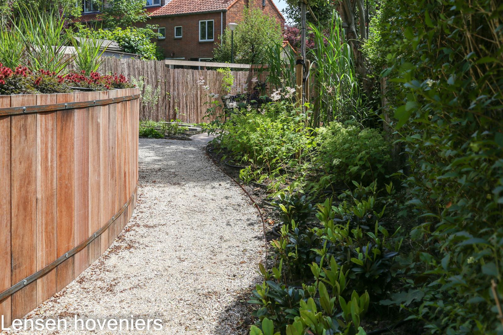 Grindpad langs een houten keerwand en hoge beplanting