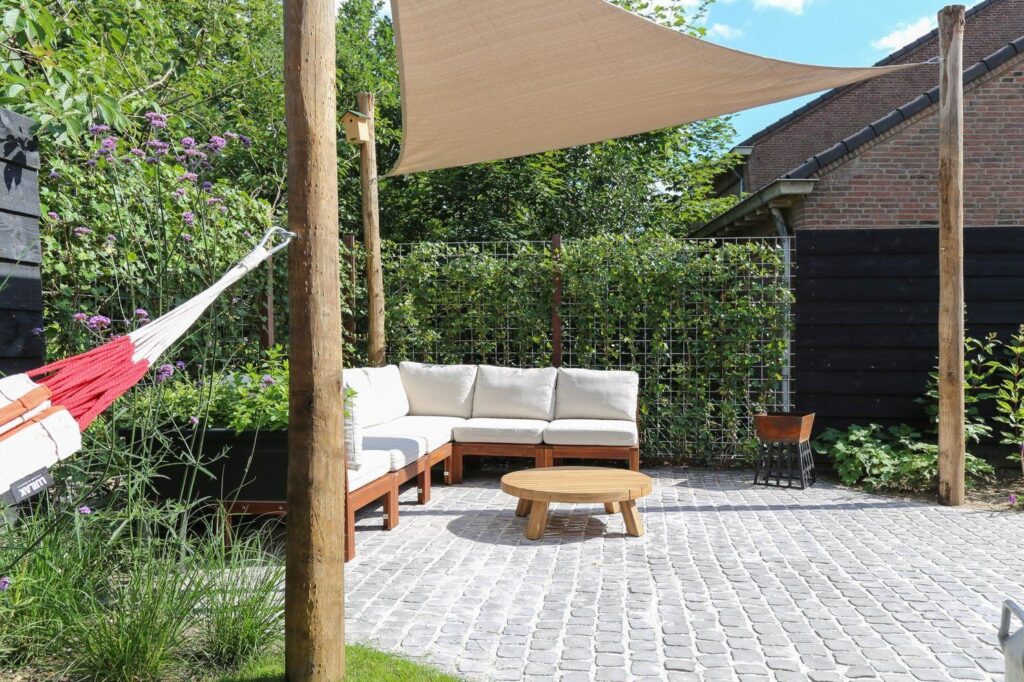 Loungebank onder een zandkleurig schaduwdoek aan kastanjehouten palen, in een kleine tuin in Oosterbeek