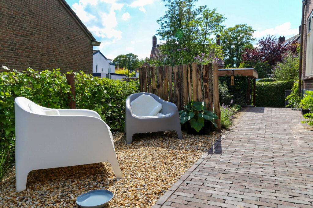 Witte loungestoelen op grind langs een klinkerpad in een kleine tuin in Oosterbeek