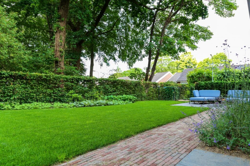 Klinkerpad en gazon met loungeset onder hoge bomen in Renkum