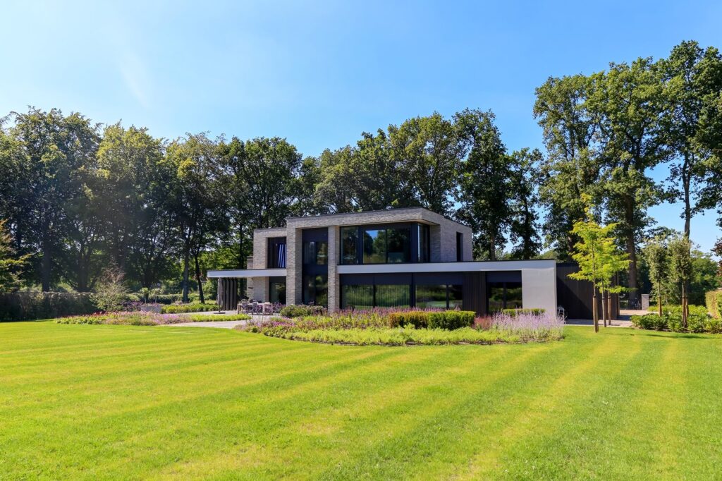 Groot gazon met maaibanen voor een villa tussen hoge bomen in Oosterbeek