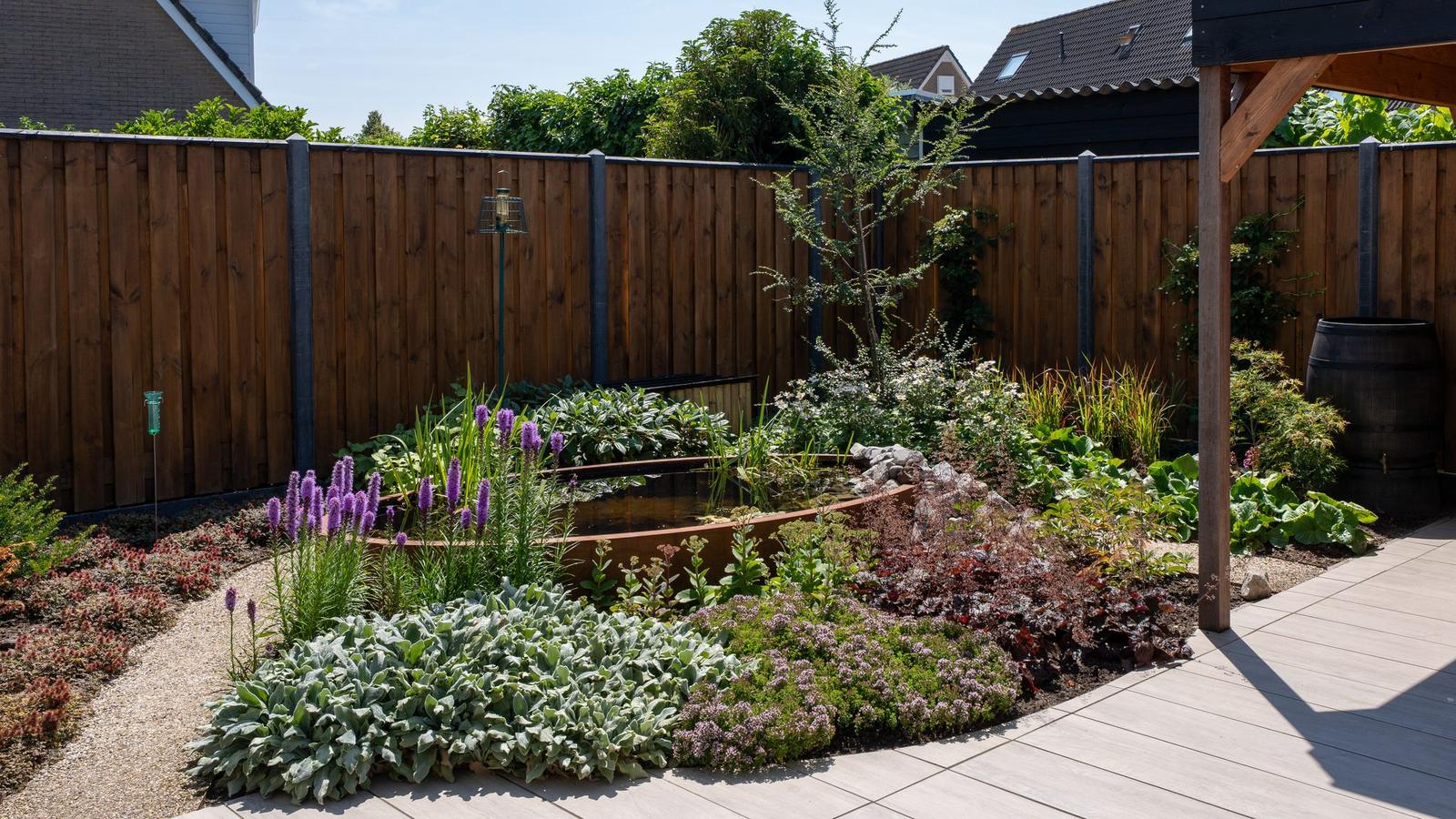 Kleine groene achtertuin met border, schutting en regenton